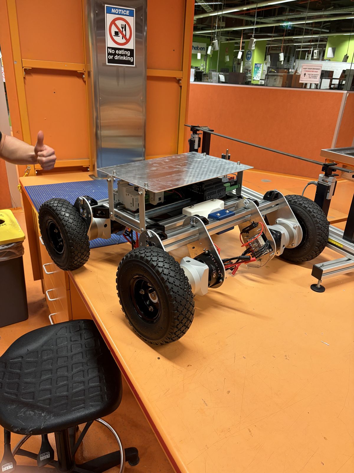 The bare Prototype 2 chassis on a workbench: aluminium extrusion frame, four pneumatic wheels, motor and gearbox units at each wheel, and a perforated top plate.