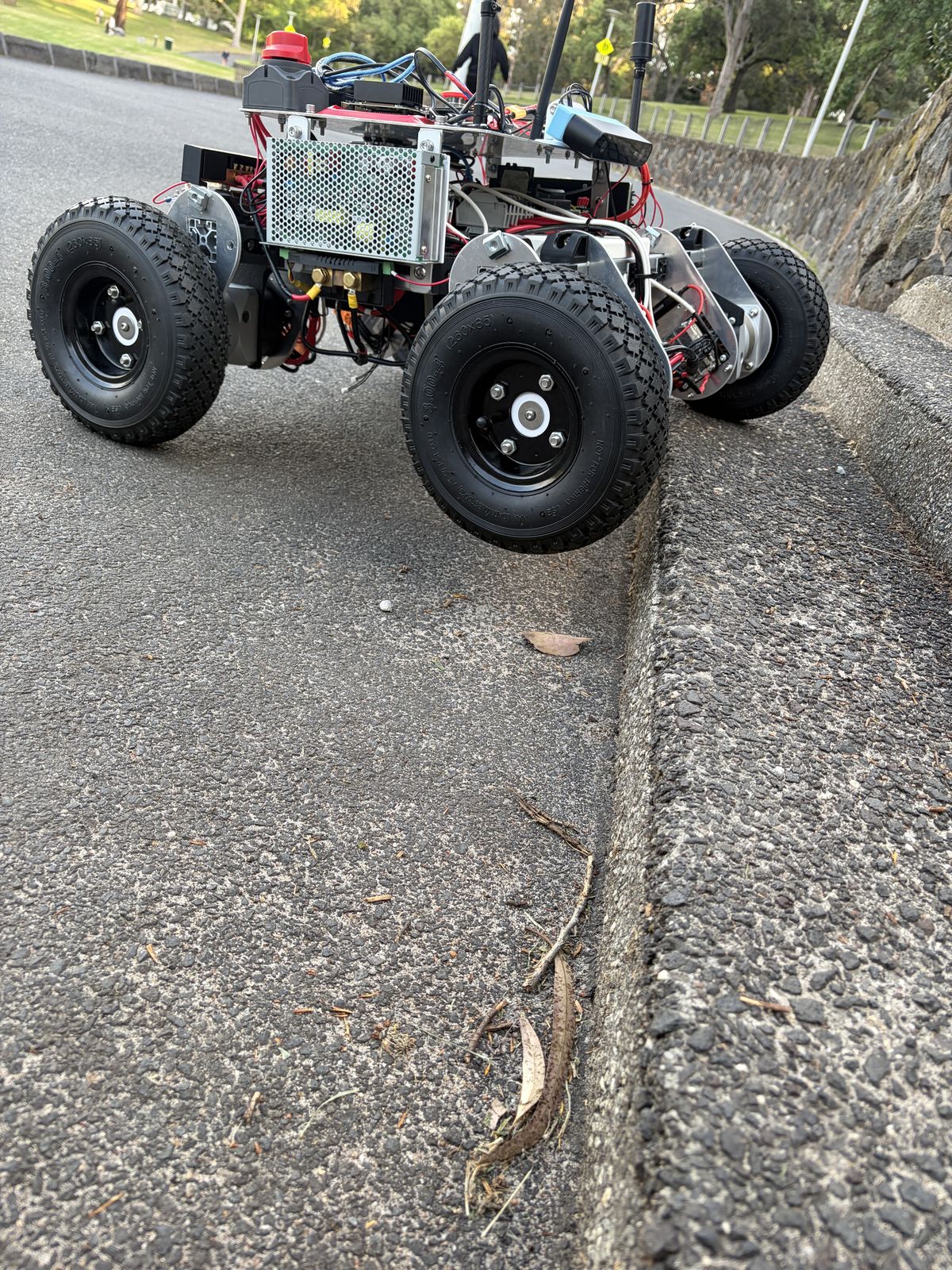 Low view of Prototype 2 on an asphalt path beside a kerb, showing the wheels and the power supply on its side.
