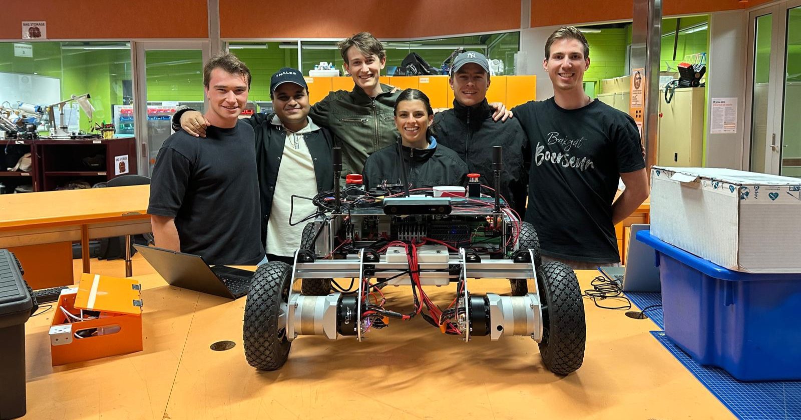 The six team members standing in the RMIT lab behind Prototype 2 on a workbench.